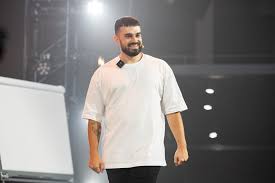 Fabio Serna como ponente sonriente en escenario iluminado con micrófono de solapa y pizarra de fondo durante evento formativo